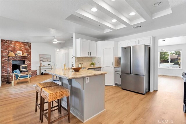 kitchen with stainless steel refrigerator, white cabinetry, kitchen peninsula, a breakfast bar area, and light wood-type flooring