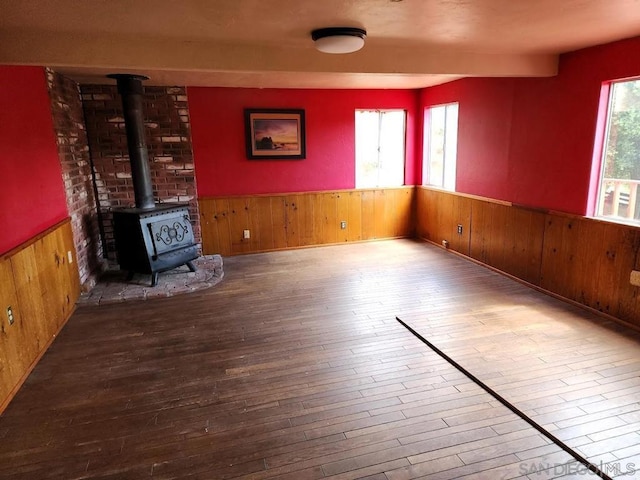 unfurnished living room featuring a wood stove, hardwood / wood-style floors, and wooden walls