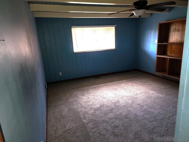 empty room with ceiling fan, carpet, and wooden walls