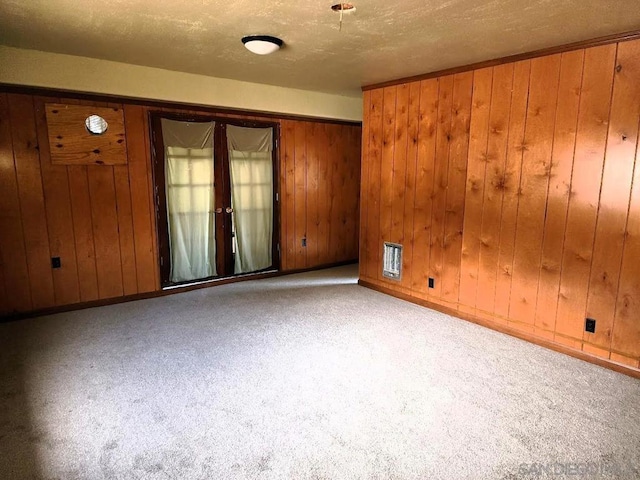 empty room featuring light carpet, french doors, wood walls, and a textured ceiling