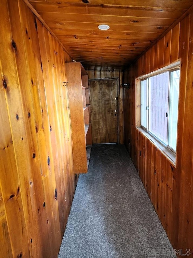 corridor with wood ceiling, wooden walls, and dark colored carpet