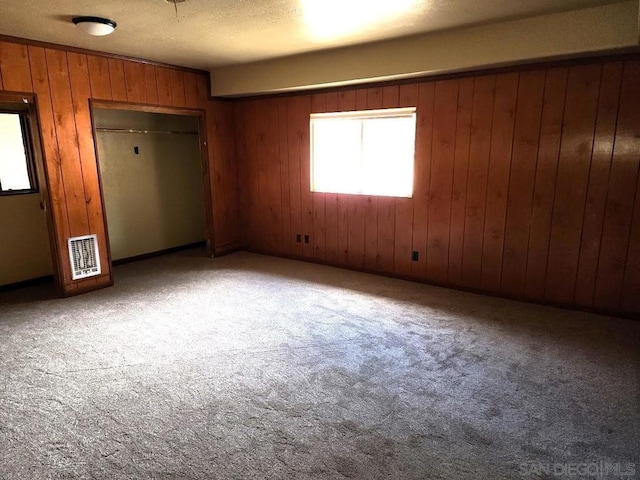 unfurnished bedroom with carpet floors, a closet, and wooden walls