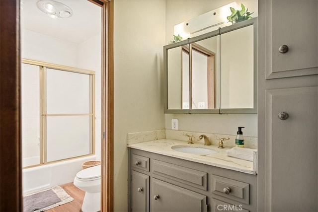 full bathroom featuring toilet, bath / shower combo with glass door, hardwood / wood-style flooring, and vanity