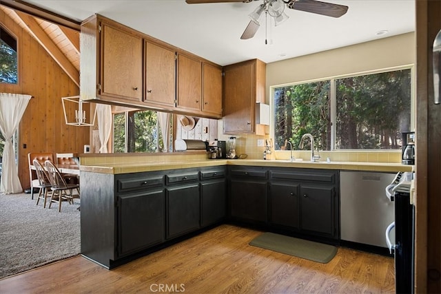 kitchen featuring stainless steel dishwasher, wooden walls, light hardwood / wood-style floors, and plenty of natural light