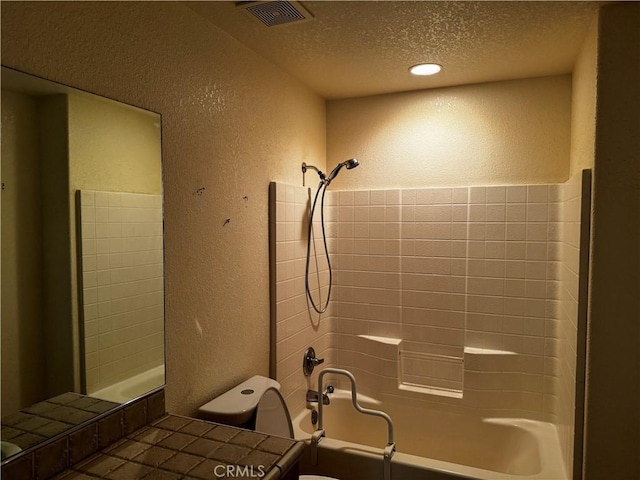 bathroom featuring toilet, a textured ceiling, and tiled shower / bath