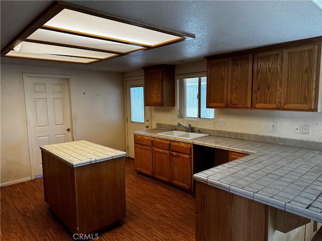 kitchen featuring sink, a center island, dark hardwood / wood-style flooring, tile countertops, and a textured ceiling