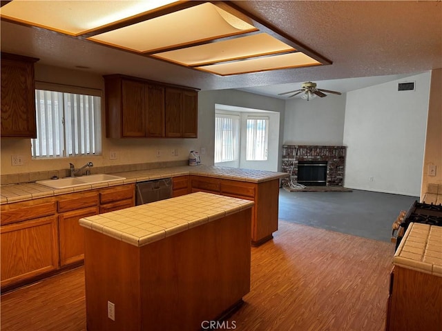 kitchen featuring tile countertops, stainless steel dishwasher, kitchen peninsula, and sink