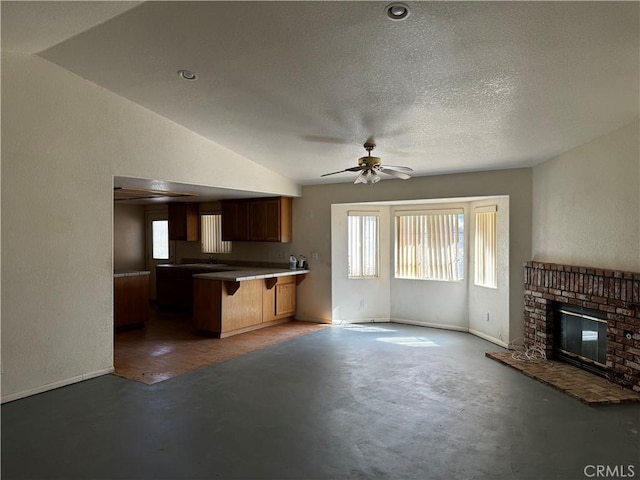 unfurnished living room featuring vaulted ceiling, ceiling fan, a textured ceiling, and a brick fireplace