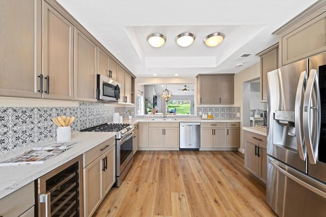 kitchen featuring tasteful backsplash, a tray ceiling, light wood-type flooring, stainless steel appliances, and beverage cooler