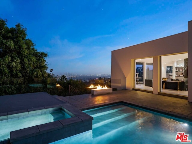 pool at dusk featuring an in ground hot tub and a patio