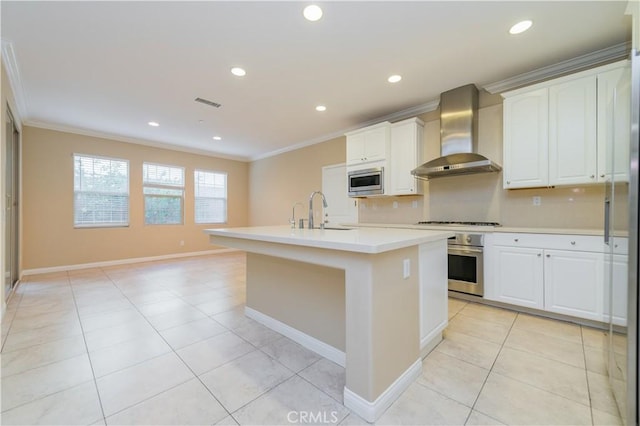 kitchen featuring wall chimney exhaust hood, sink, stainless steel appliances, a kitchen island with sink, and white cabinets