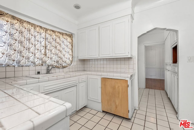 kitchen featuring decorative backsplash, white cabinetry, tile countertops, and light tile patterned floors