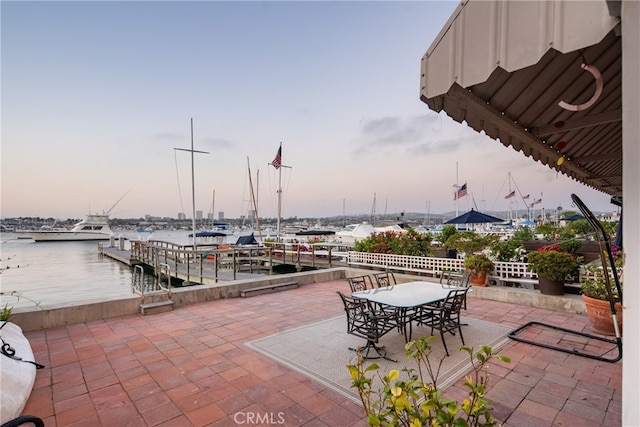 patio terrace at dusk featuring a dock and a water view