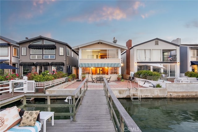 back house at dusk featuring a balcony and a water view