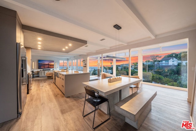 kitchen with beamed ceiling, hanging light fixtures, a center island with sink, light hardwood / wood-style flooring, and a breakfast bar