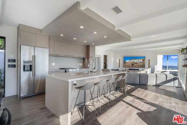 kitchen with gray cabinetry, a large island with sink, appliances with stainless steel finishes, a breakfast bar, and light wood-type flooring