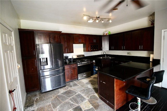 kitchen featuring ceiling fan, sink, kitchen peninsula, stainless steel appliances, and a breakfast bar area