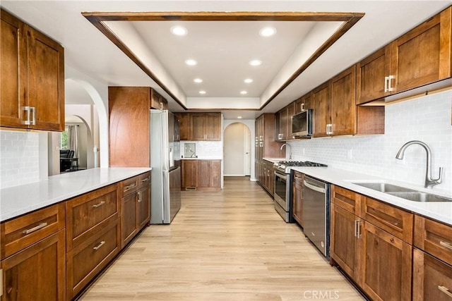 kitchen featuring sink, backsplash, stainless steel appliances, light hardwood / wood-style floors, and a raised ceiling