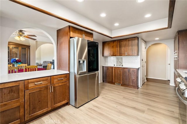 kitchen with stainless steel appliances, a tray ceiling, backsplash, and light hardwood / wood-style flooring