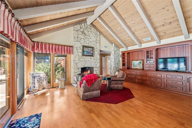 living room with wood ceiling, light hardwood / wood-style floors, a stone fireplace, and beamed ceiling