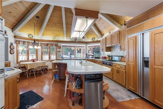 kitchen with tasteful backsplash, pendant lighting, lofted ceiling with beams, sink, and a kitchen island with sink