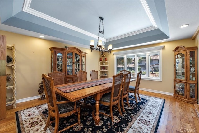 dining space with crown molding, an inviting chandelier, a tray ceiling, and light hardwood / wood-style flooring