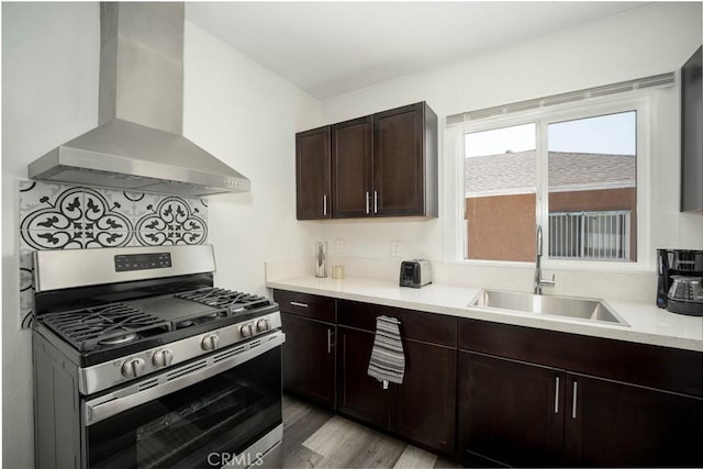 kitchen featuring extractor fan, stainless steel gas range, dark brown cabinets, light hardwood / wood-style flooring, and sink