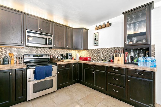 kitchen featuring dark brown cabinets, stainless steel appliances, sink, light stone counters, and tasteful backsplash