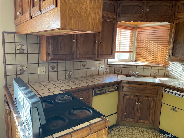 kitchen featuring backsplash, white dishwasher, sink, and tile counters