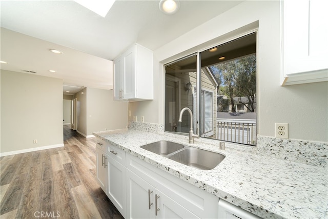 kitchen with wood-type flooring, white cabinetry, sink, and light stone countertops