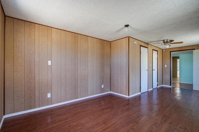 unfurnished room with ceiling fan, wood walls, a textured ceiling, and dark hardwood / wood-style flooring