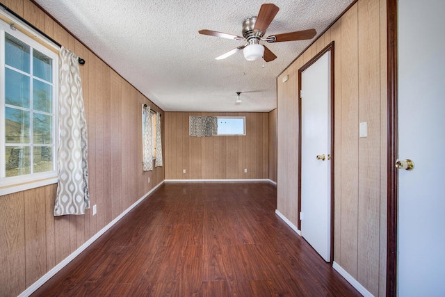 empty room featuring wooden walls, ceiling fan, a textured ceiling, and dark hardwood / wood-style flooring