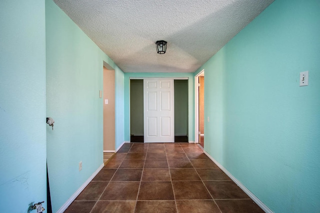 corridor featuring a textured ceiling and dark tile patterned flooring