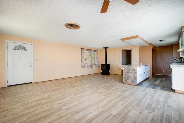 unfurnished living room featuring light hardwood / wood-style floors, a wood stove, a textured ceiling, and ceiling fan