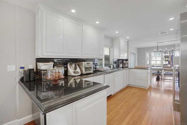 kitchen featuring white cabinets, light hardwood / wood-style floors, kitchen peninsula, and a chandelier