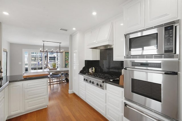 kitchen featuring white cabinetry, stainless steel appliances, light wood-type flooring, an inviting chandelier, and custom exhaust hood