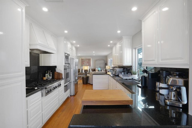 kitchen featuring appliances with stainless steel finishes, white cabinetry, backsplash, kitchen peninsula, and light hardwood / wood-style flooring