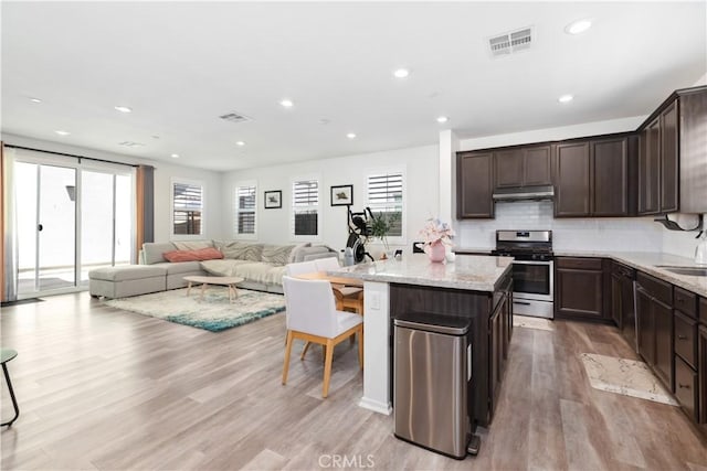 kitchen featuring stainless steel gas stove, light hardwood / wood-style flooring, light stone countertops, a kitchen island, and dark brown cabinetry