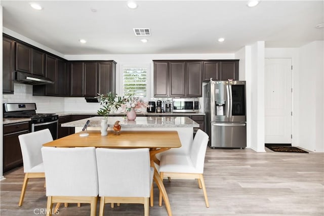 kitchen with dark brown cabinets, light hardwood / wood-style flooring, appliances with stainless steel finishes, a kitchen island, and decorative backsplash