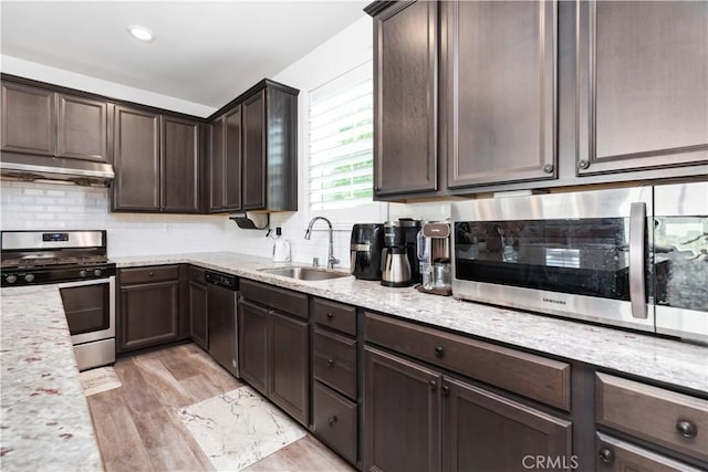 kitchen with sink, stainless steel appliances, light stone counters, light hardwood / wood-style floors, and dark brown cabinetry