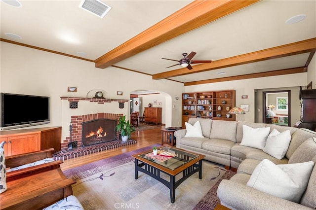 living room with a brick fireplace, ceiling fan, hardwood / wood-style floors, and beamed ceiling