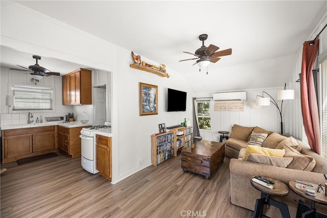 living room with lofted ceiling, ceiling fan, an AC wall unit, light hardwood / wood-style floors, and sink