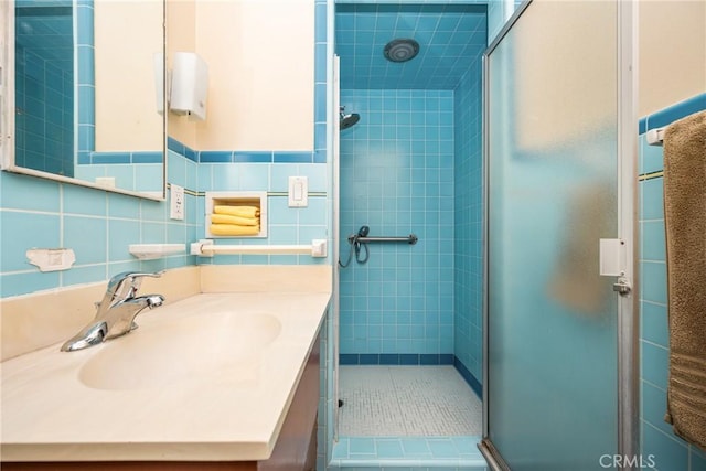 bathroom with tile patterned flooring, tile walls, a shower with door, and vanity