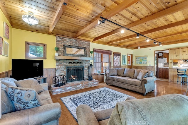 living room featuring beamed ceiling, wooden walls, wood-type flooring, and rail lighting