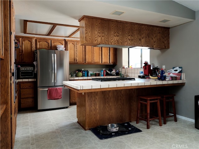 kitchen with a breakfast bar area, kitchen peninsula, tile countertops, and stainless steel refrigerator