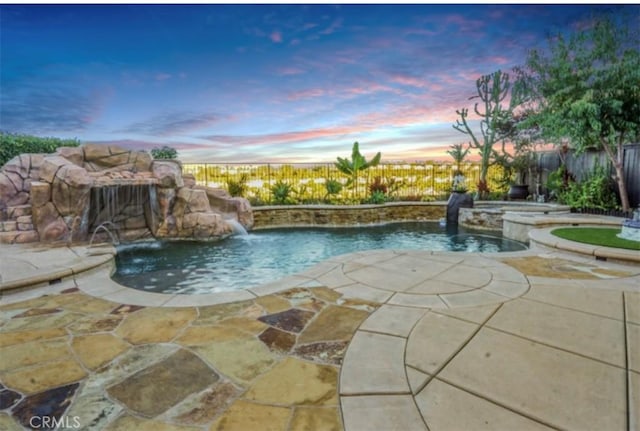 pool at dusk featuring pool water feature and a patio area