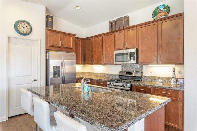 kitchen featuring sink, an island with sink, appliances with stainless steel finishes, light hardwood / wood-style floors, and a kitchen bar