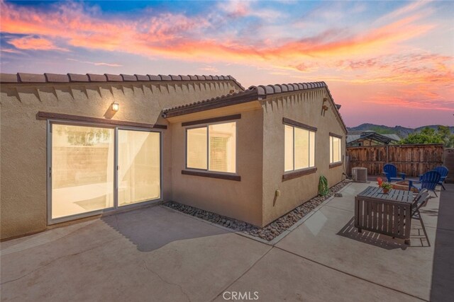 back house at dusk with a patio area, an outdoor living space, and central AC