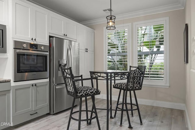 kitchen featuring white cabinets, decorative light fixtures, stainless steel appliances, light wood-type flooring, and crown molding