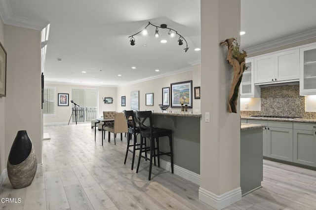 kitchen featuring light wood-type flooring, light stone counters, a breakfast bar, white cabinets, and crown molding